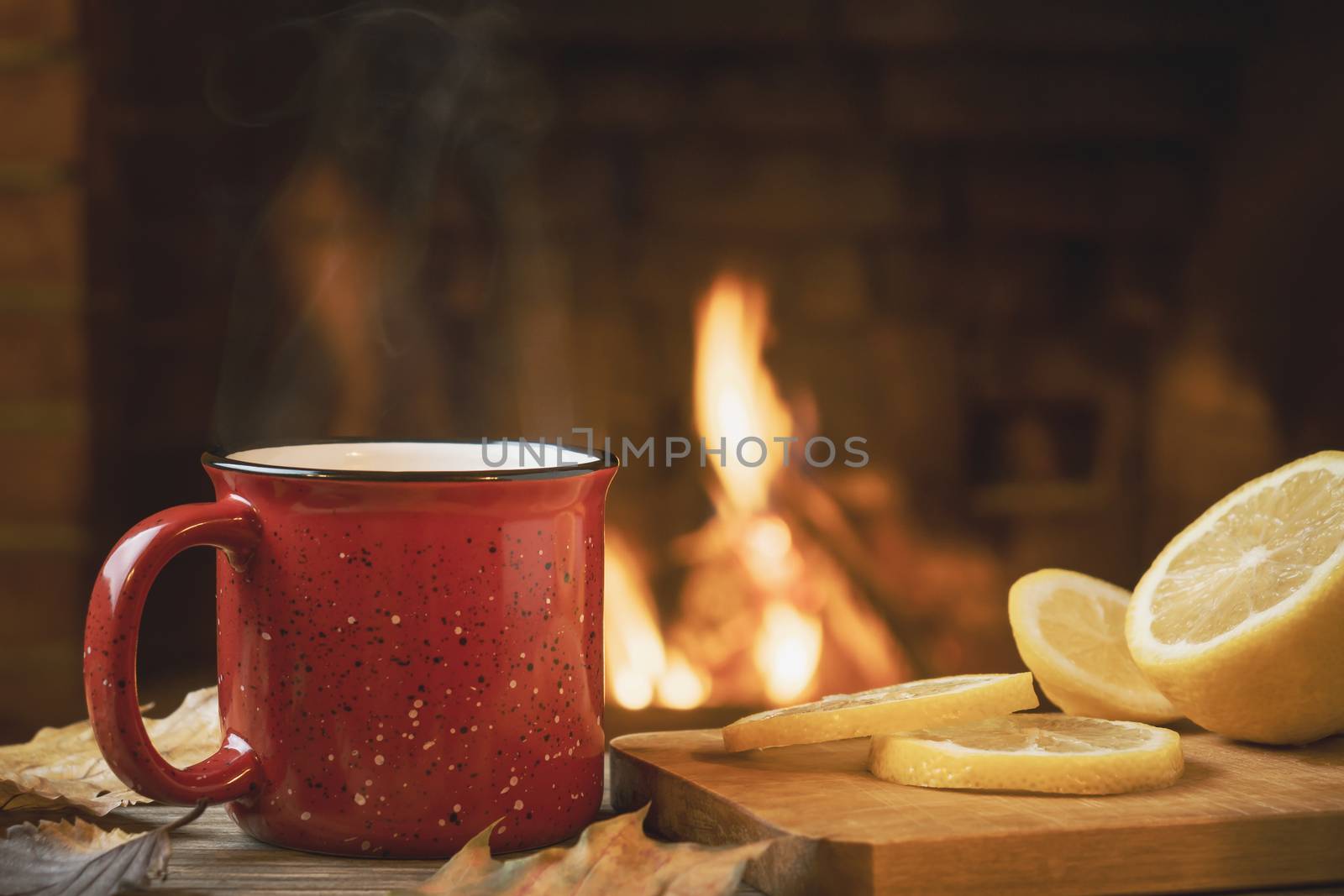 Red mug with hot tea with lemon in front of a burning fireplace, comfort and warmth of the hearth concept by galsand