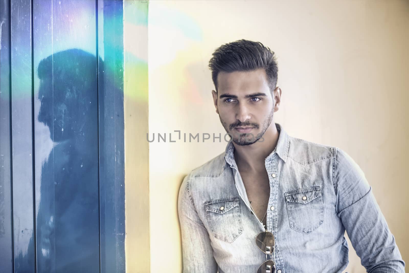 Attractive young man standing against colorful wall, looking at camera, wearing denim shirt