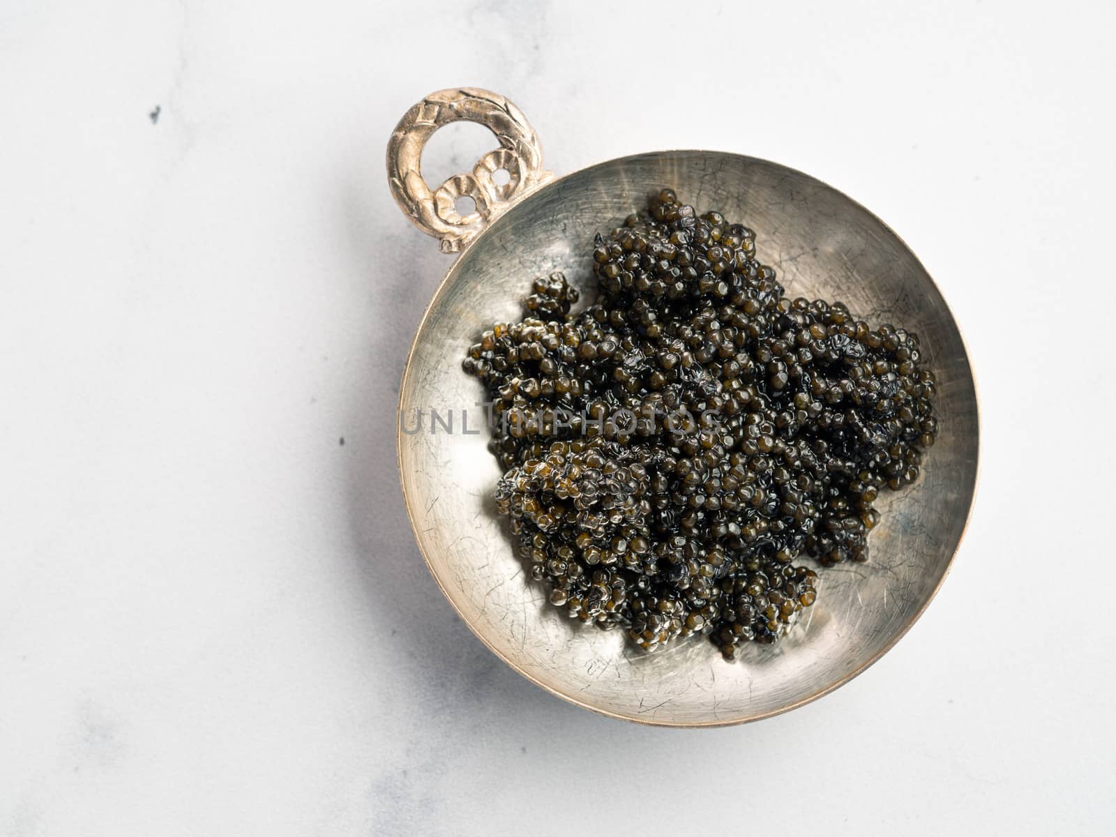 Black caviar top view or flat lay. Bowl of black caviar on white marble background. Copy space for text.