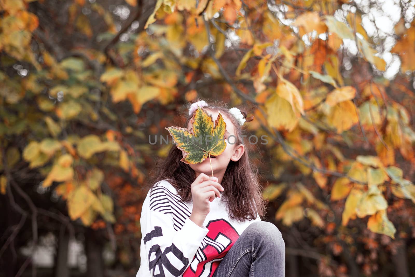 Girl holding colorful leaf in autumn park.