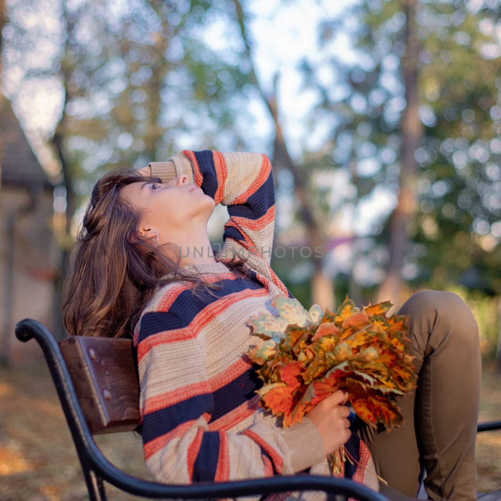 In the girl's hand holds autumn leaves.Beautiful girl sits on a bench in autumn.