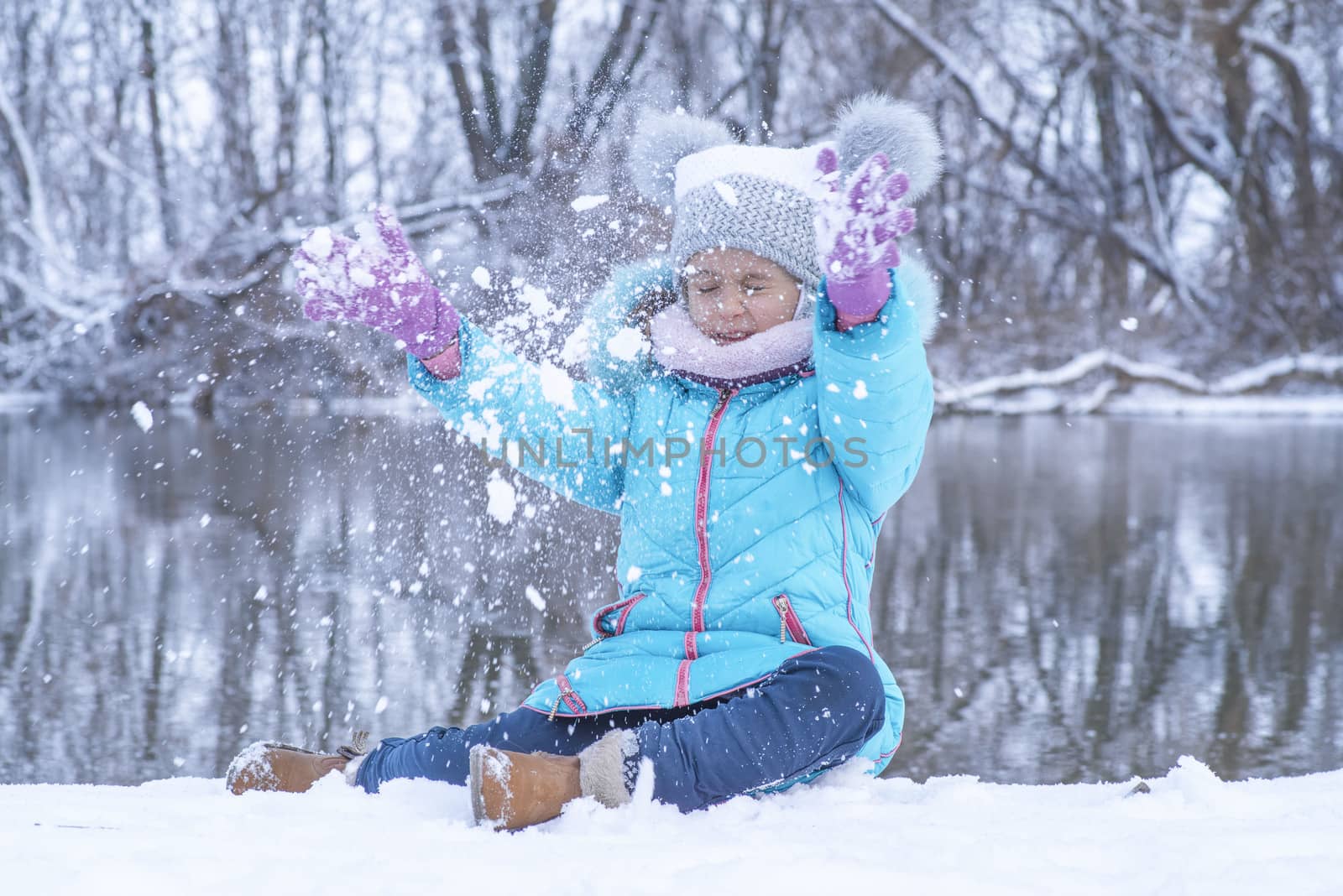 Children play outside in the winter. Snow games in the street.A little girl in a charcoal jacket plays in the winter on the street with snow.