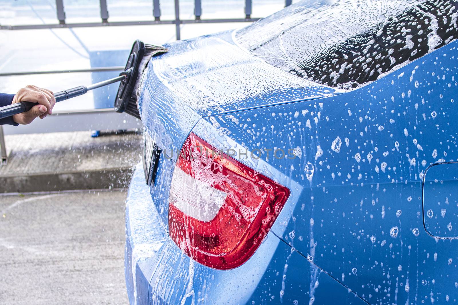 Manual car wash with pressurized water in car wash outside.Using a brush to wash a car on a car washing facility on sunny summer day.Blue car manual wash of with pressurized water in car wash outside.