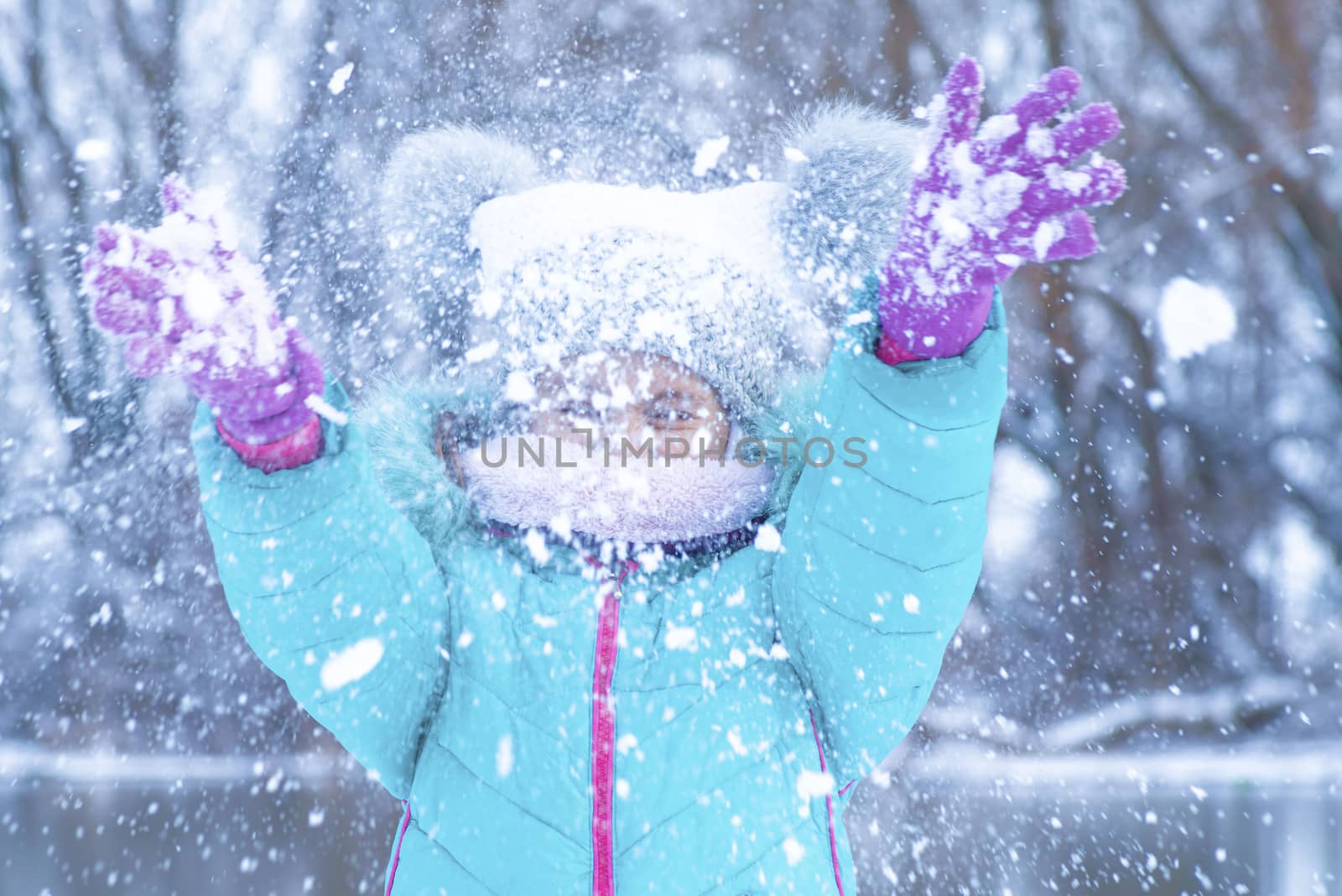 Children play outside in the winter. Snow games in the street.A little girl in a charcoal jacket plays in the winter on the street with snow.