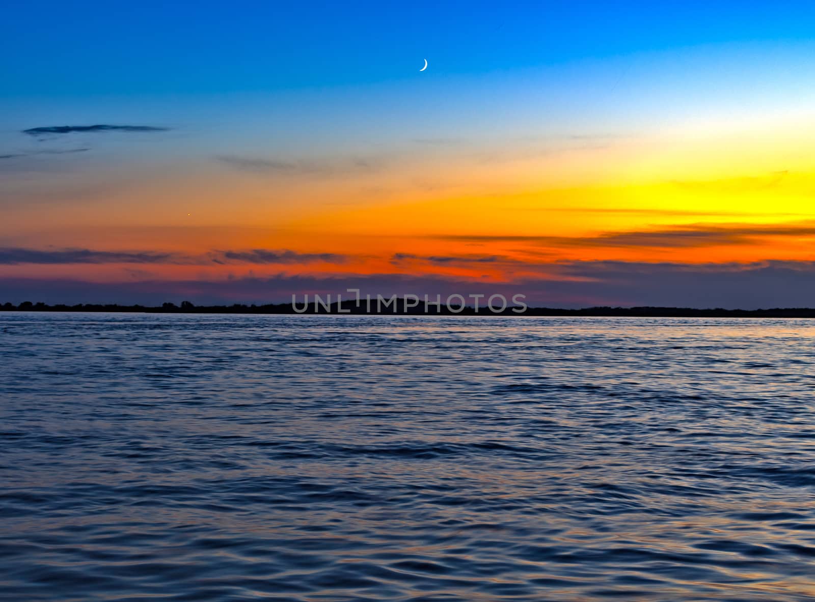 Sunset on the embankment of the Amur river in Khabarovsk. The sun set over the horizon. The embankment is lit by lanterns. People walk along the river Bank.