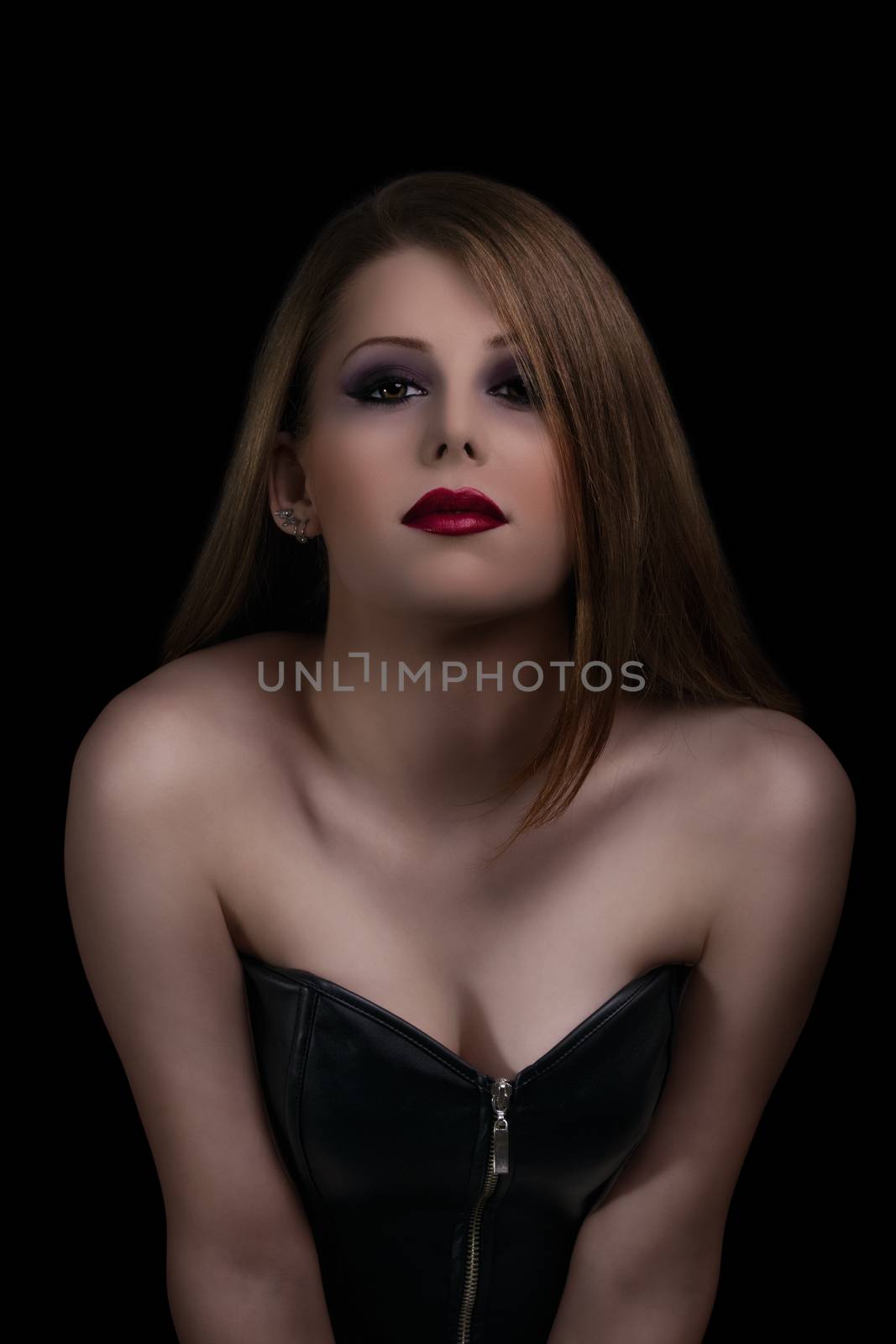 Low key make up and beauty portrait of a sensual young woman with red lipstick on black background.