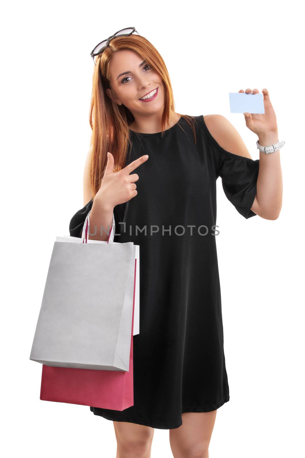 Portrait of a beautiful young girl in a stylish dress holing shopping bags and pointing to a blank card, isolated on white background. Shopping concept, copy space.
