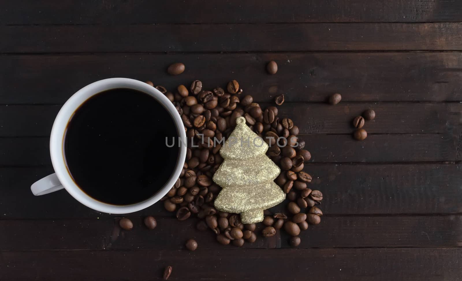 Cup of coffee with coffee beans and toy Christmas tree on wooden background.Christmas and new year concept.Copyspace.