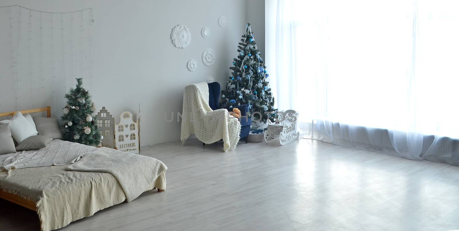 Stylish Christmas interior with a chair and an elegant sofa. Comfort home. Presents and wrapped gifts under the Christmas tree and bauble in sunny living room.