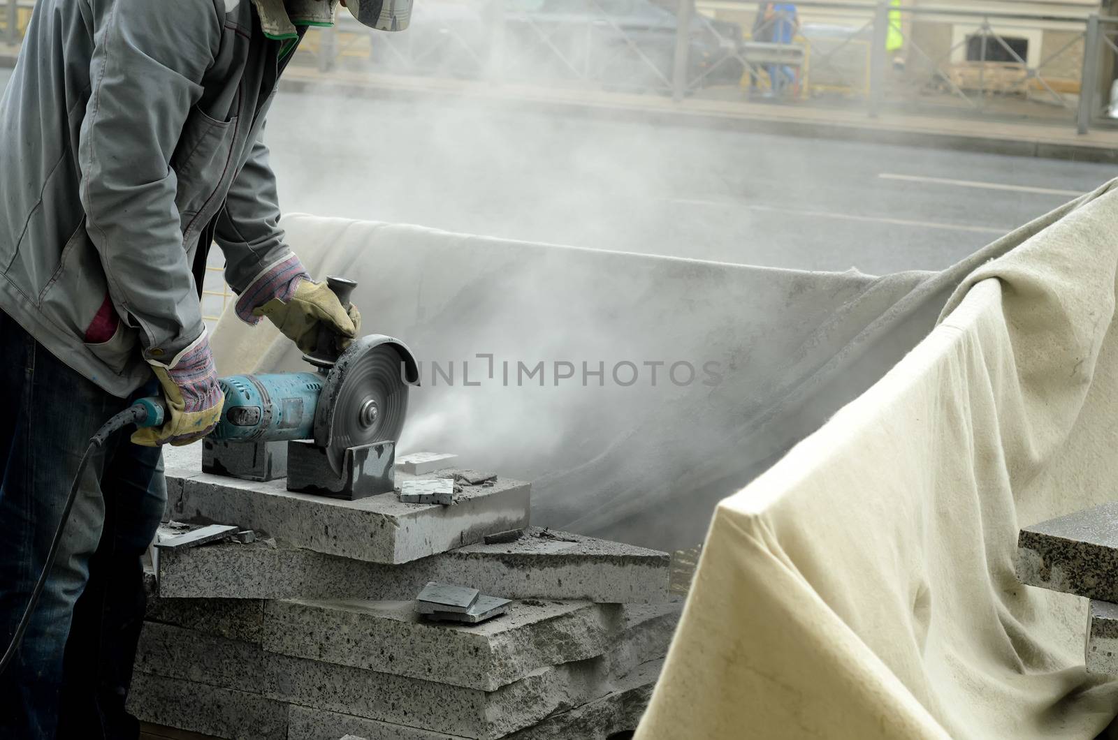 The worker cuts a big powerful angle grinder paving slabs on the street.