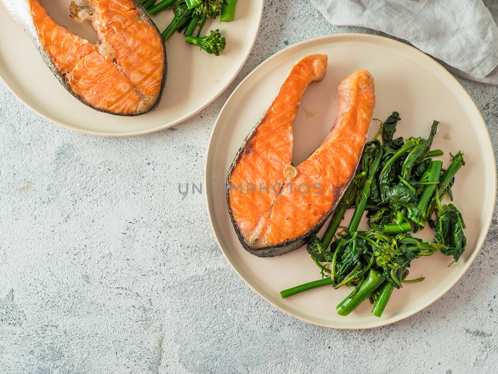 Ready-to-eat grilled salmon steak and greens - baby broccoli or broccolini and spinach on rustic craft plate over gray background. Keto diet dish. Top view or flat lay. Copy space for text or design.