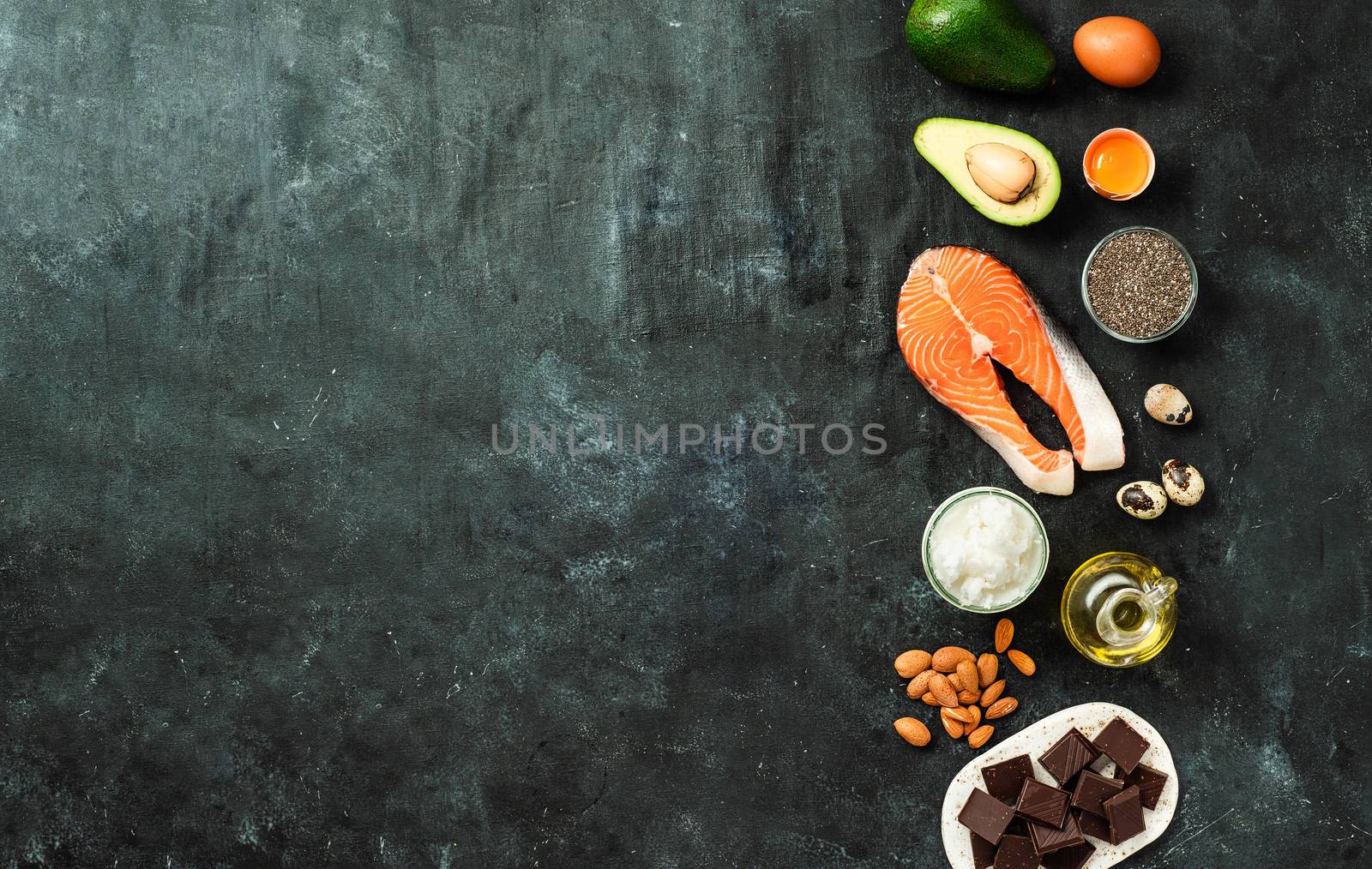 Healthy fats sources concept. Different food ingredients rich good healthy fats on dark background. Copy space left. Top view or flat lay.