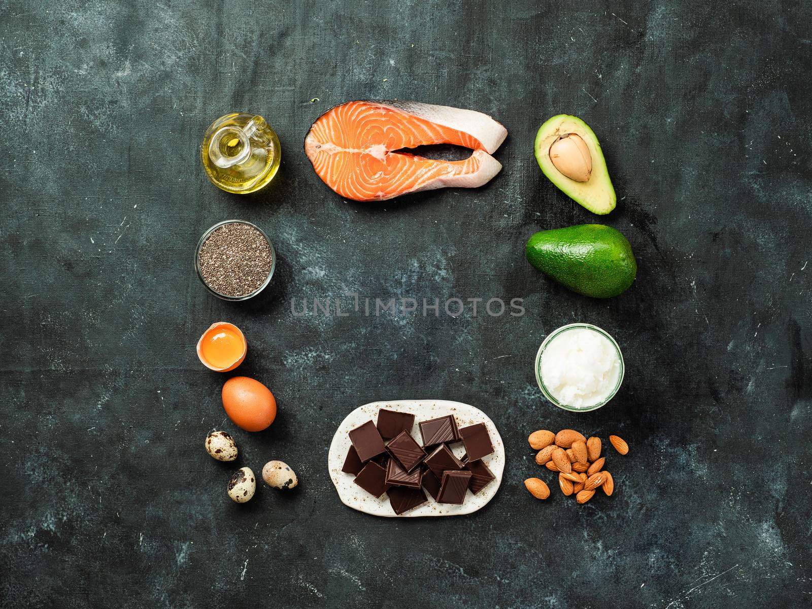 Healthy fats sources concept. Different food ingredients rich good healthy fats on dark background with copy space in center for text or design. Top view or flat lay.