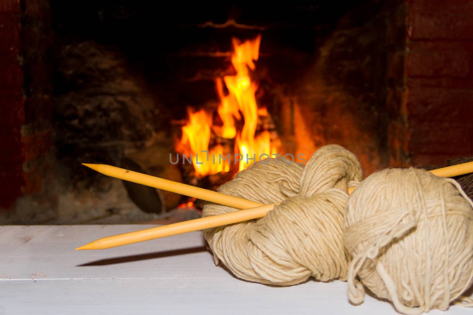 winter concept knitting wool and tricot needles with fire from home on wood background by GabrielaBertolini
