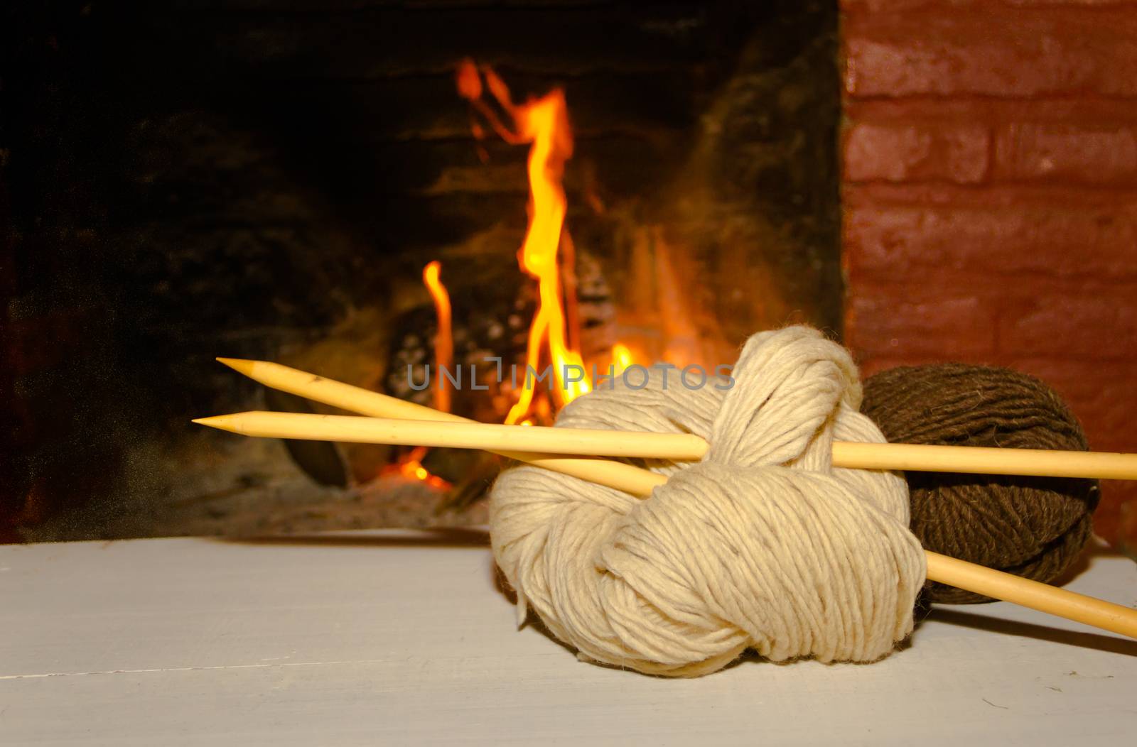 winter concept knitting wool and tricot needles with fire from home on wood background
