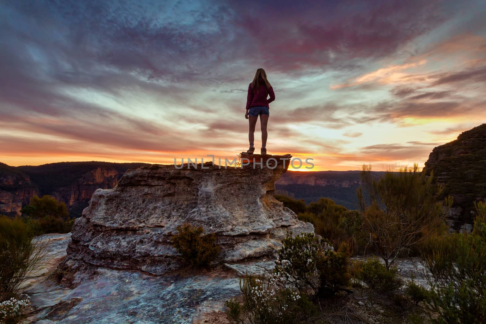 Hiker on podium like rock with wonderful views of the sandstone cliffs catching the last light of the setting sun in Blue Mountains