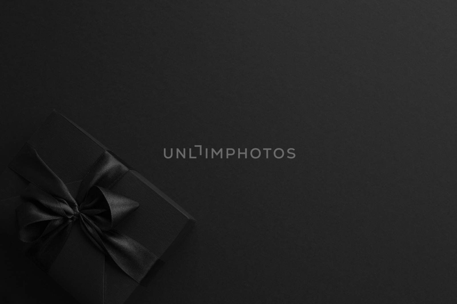 Black friday gift, paper box with silk ribbon bow on black paper background with copy space for text, flat lay top view template