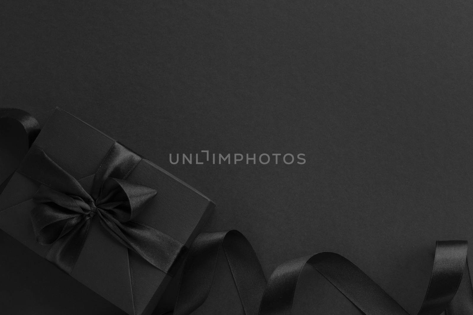 Black friday gift, paper box with silk ribbon bow on black paper background with copy space for text, flat lay top view template