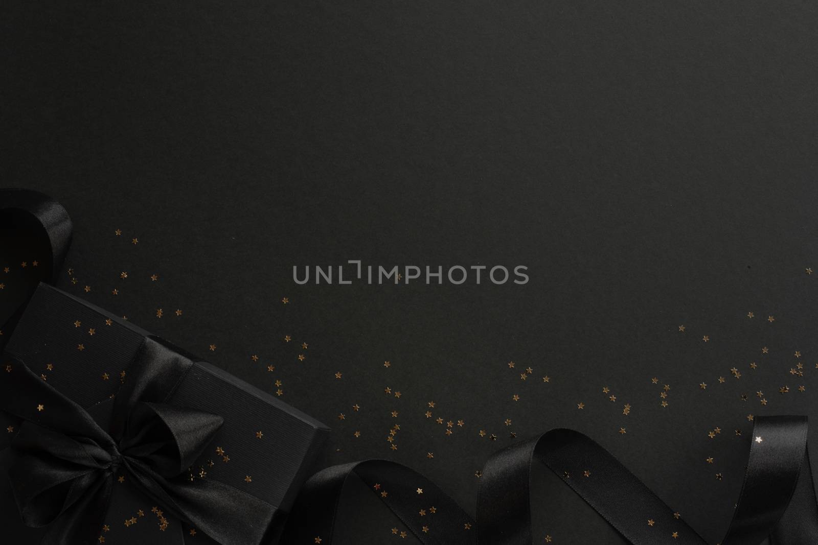 Black friday gift, paper box with silk ribbon bow and golden glitter stars on black paper background with copy space for text, flat lay top view template