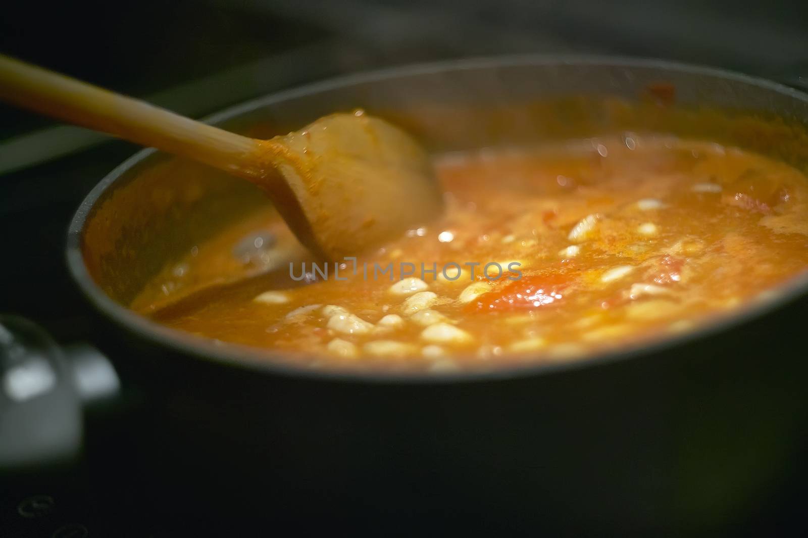 Pot of gravy or soup while cooking on the stove and is stirred to achieve the perfect cooking to be served.