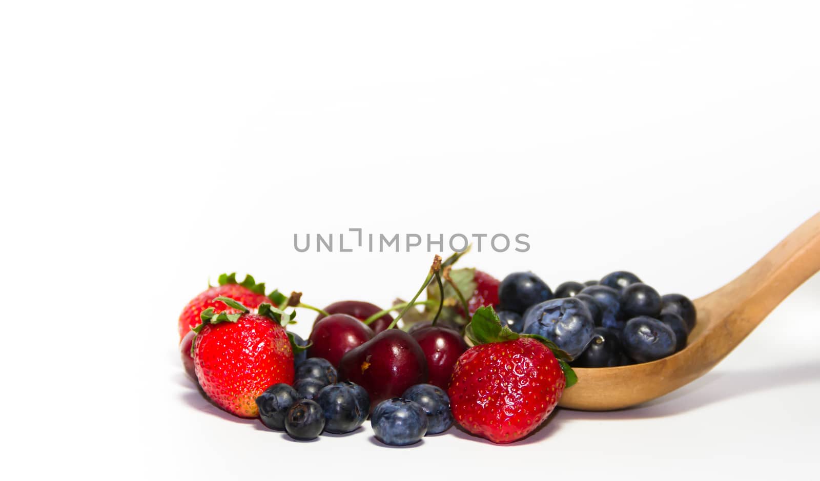 red fruits on white background and wooden spoon