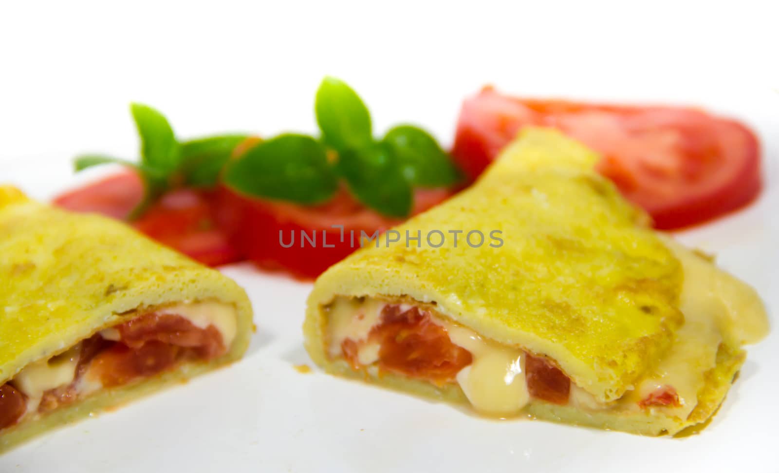 omelette made with beaten eggs stuffed with onion cheese and tomatoes on white background with sliced tomatoes and basil by GabrielaBertolini