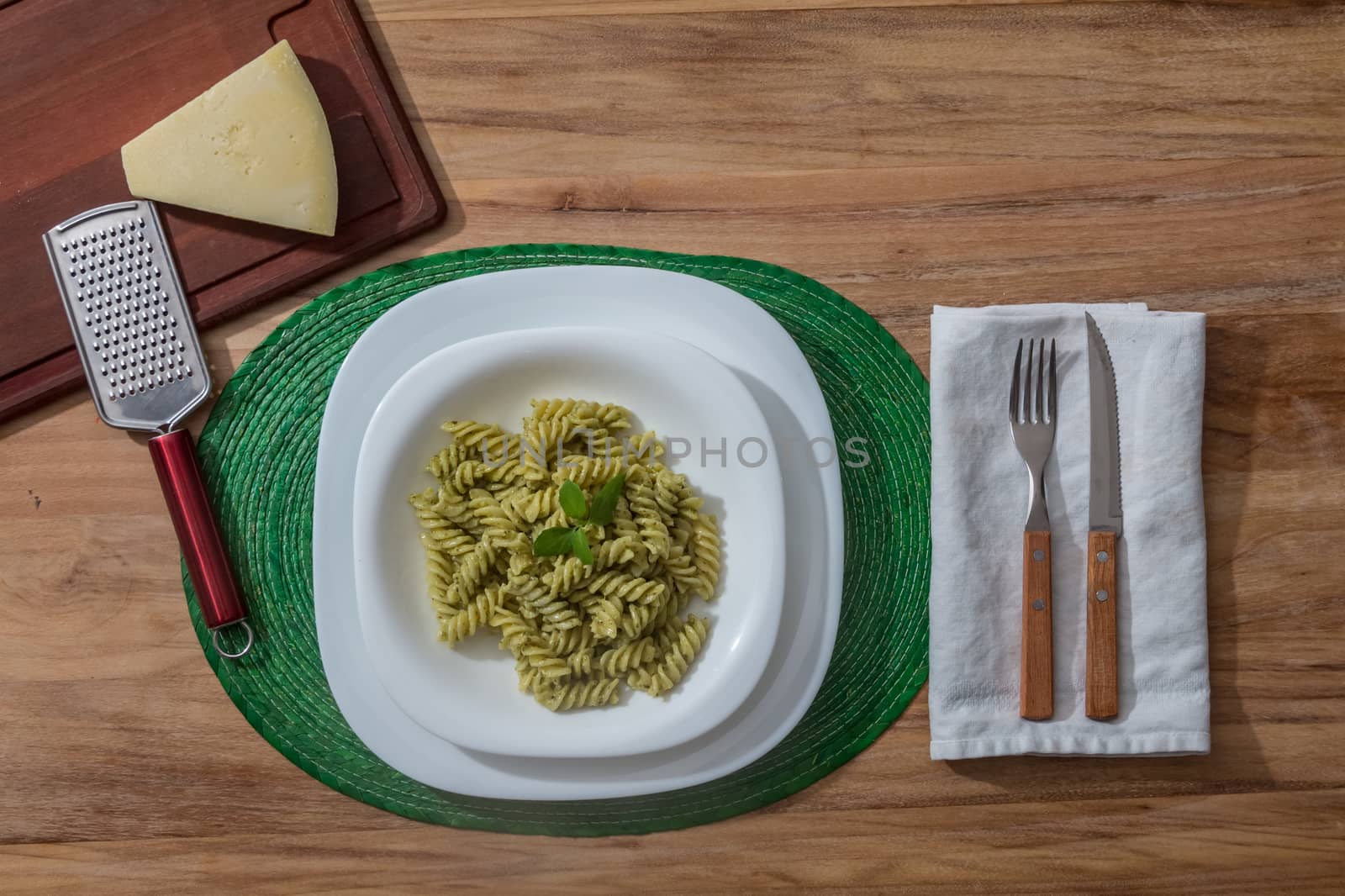 Pesto pasta in a white plate on a wooden table by leo_de_la_garza