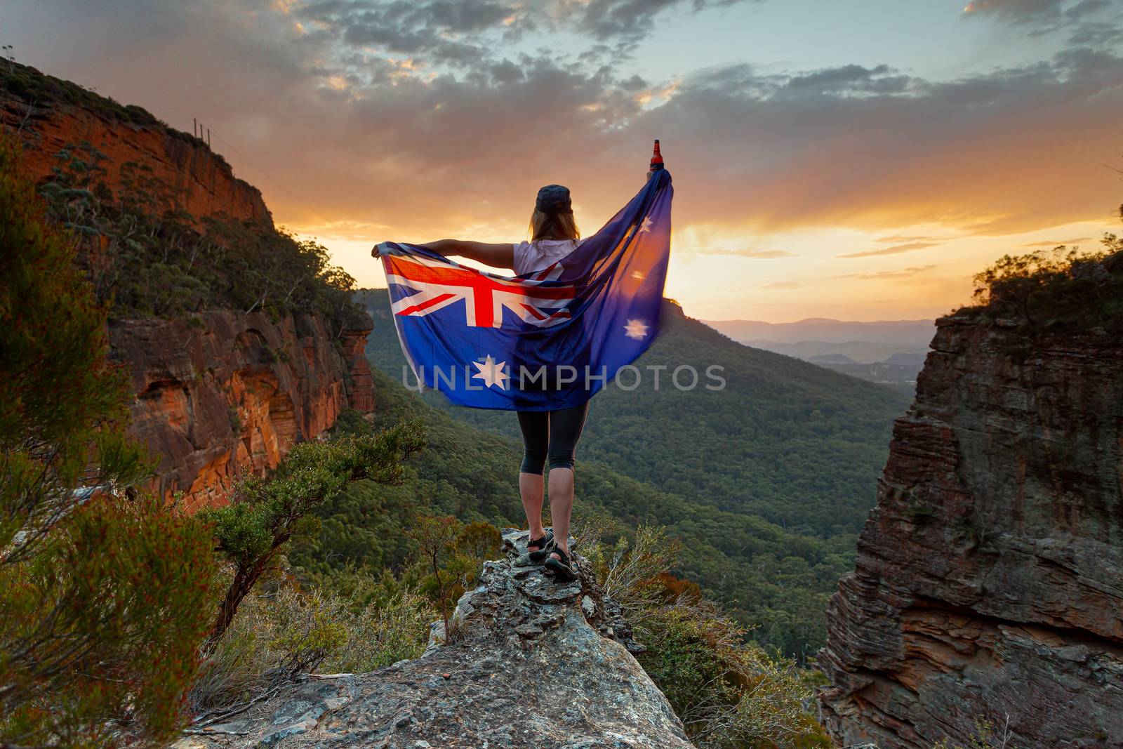 Patriotic woman holding large Australian flag in Blue Mountains Australia.  Celebrate Australia Day, Sports supporter, tourism, Australian travel, Aussie Pride themes.  Selective focus to woman only.  Flag shows some motion from wind.