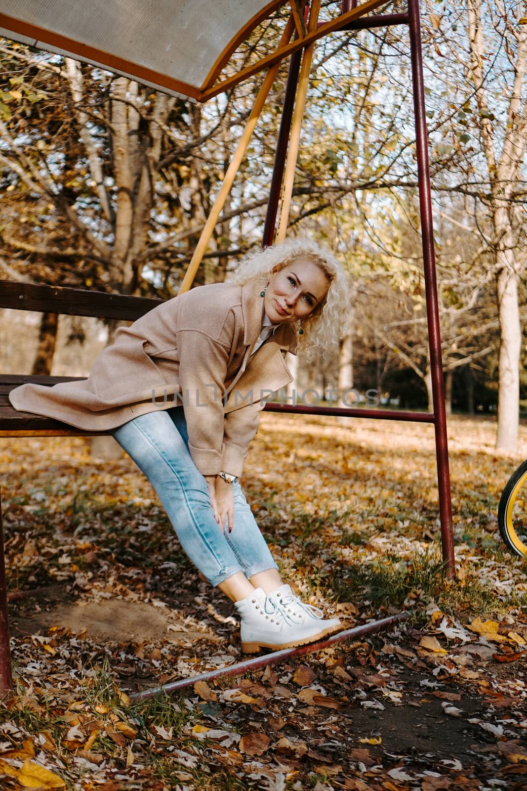 Portrait of smilling middle aged woman sitting and swinging on swing in autumn park