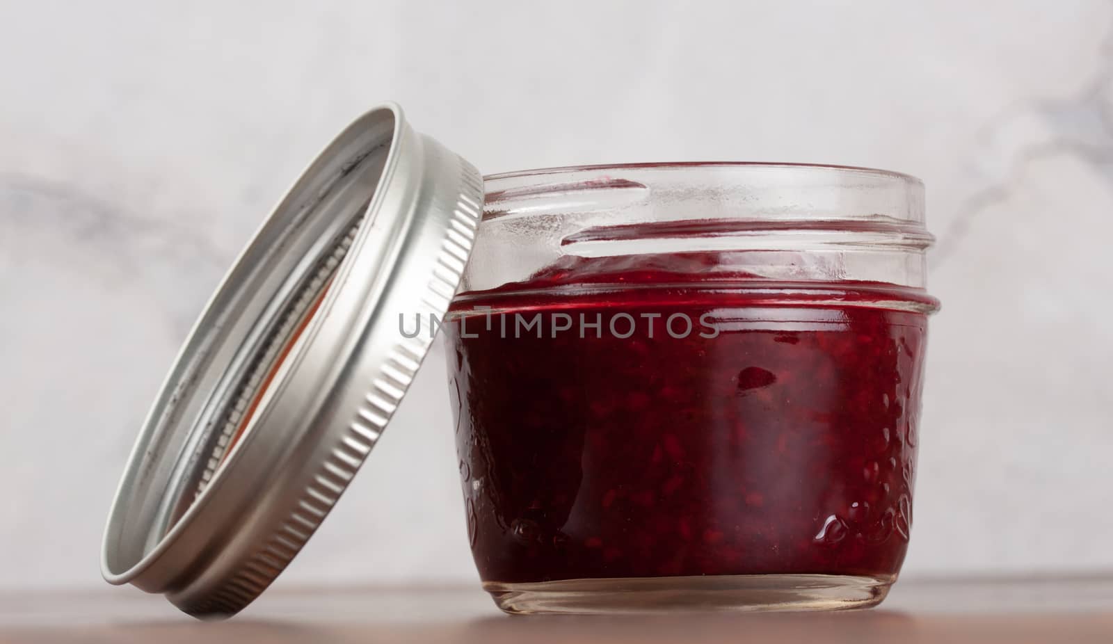 Homemade raspberry jam in a reusable glass jar by lanalanglois