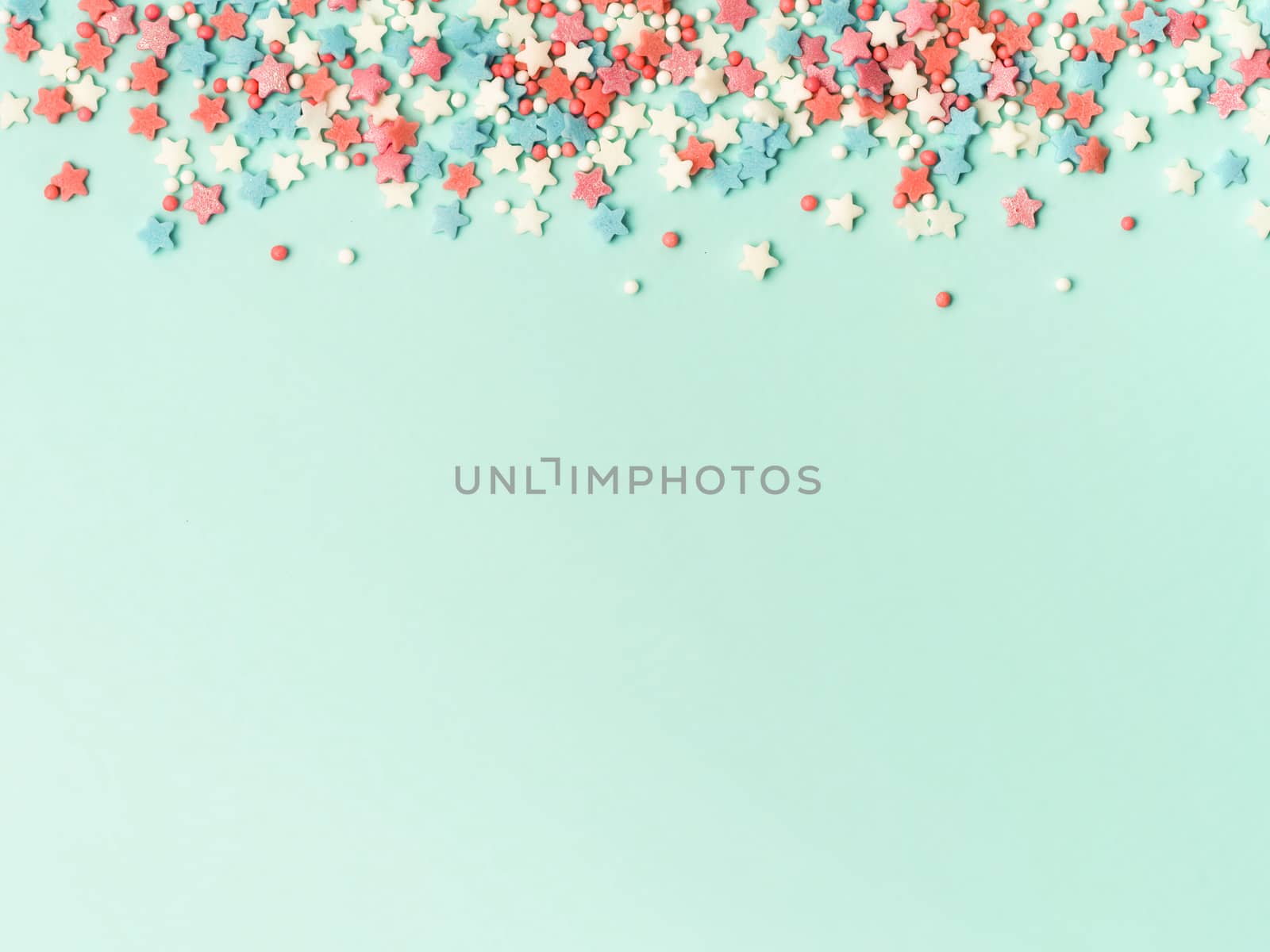 Festive border frame of colorful pastel sprinkles on blue background with copy space bottom. Sugar sprinkle dots and stars, decoration for cake and bakery. Top view or flat lay.