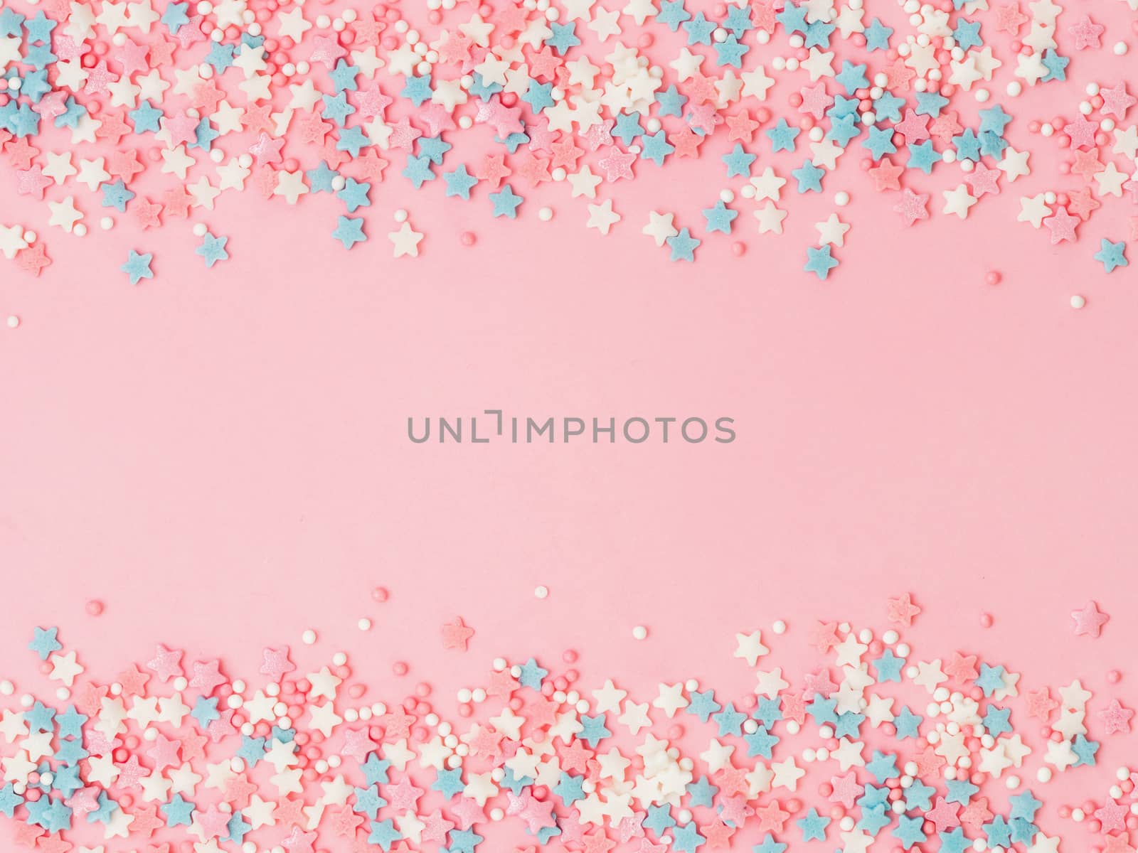 Festive border frame of colorful pastel sprinkles on pink background with copy space in center. Sugar sprinkle dots and stars, decoration for cake and bakery. Top view or flat lay