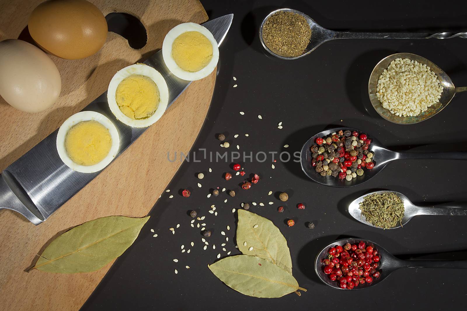 Spices in metal spoons and eggs on a cutting board