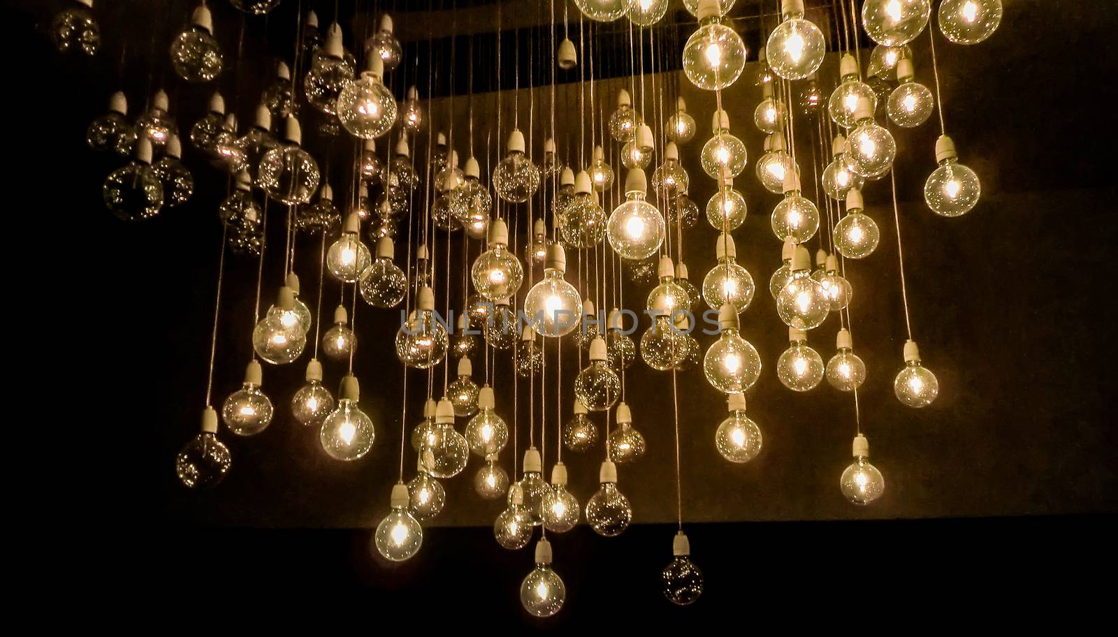 Many light bulbs hanging from wires and lit to illuminate the surrounding darkness.