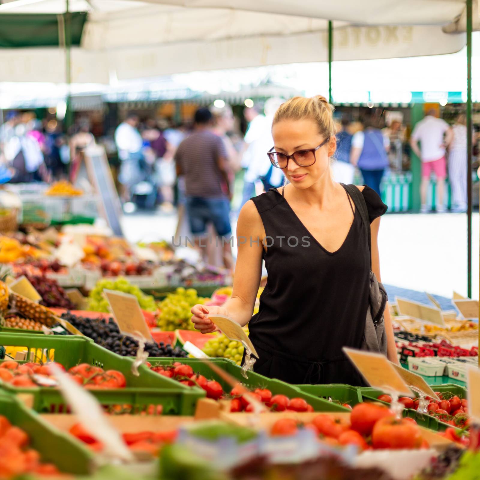 Woman buying fruits and vegetables at local food market. Market stall with variety of organic vegetable by kasto