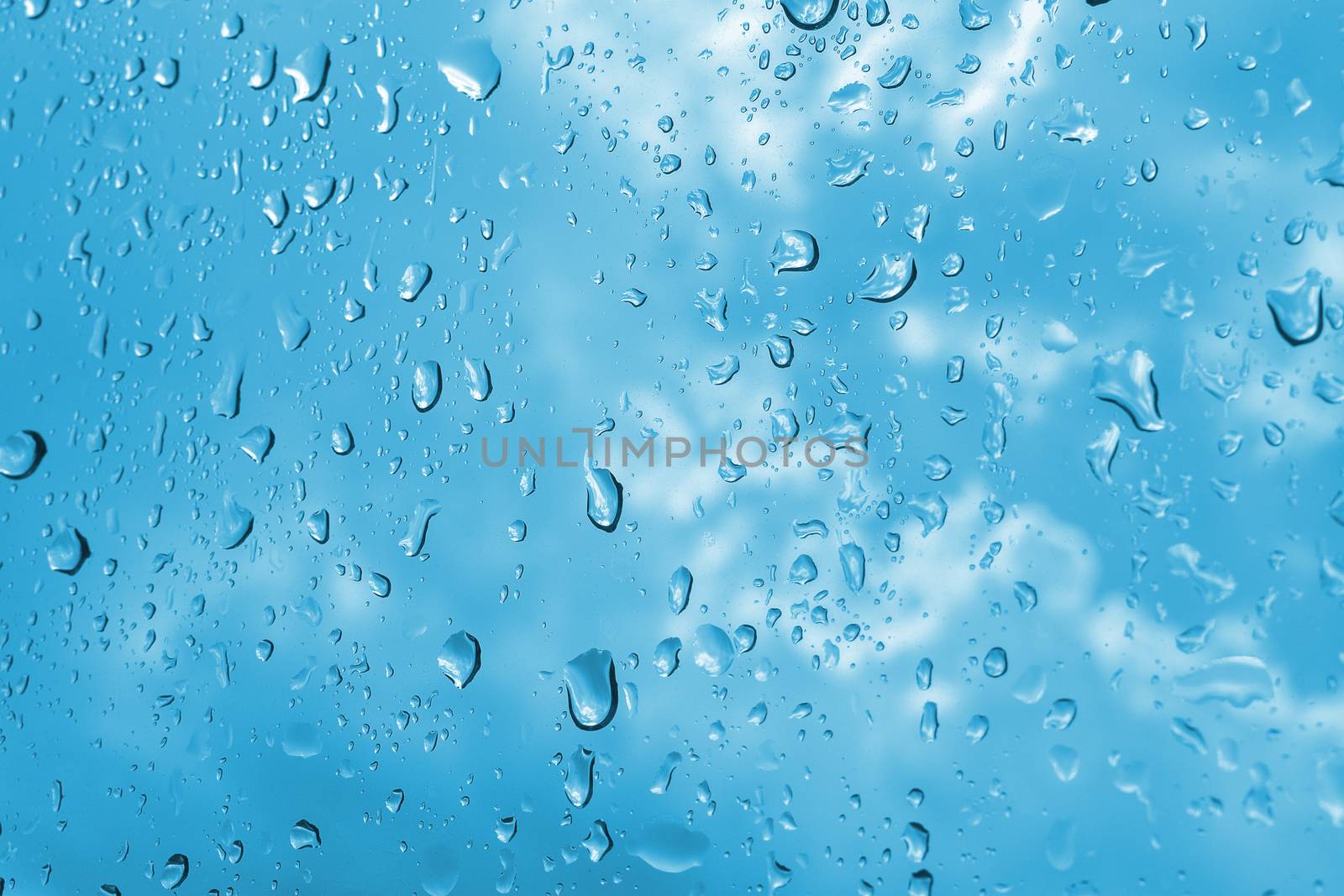 Closeup raindrops in the window glass. Cloudy blue sky in the background. Macro