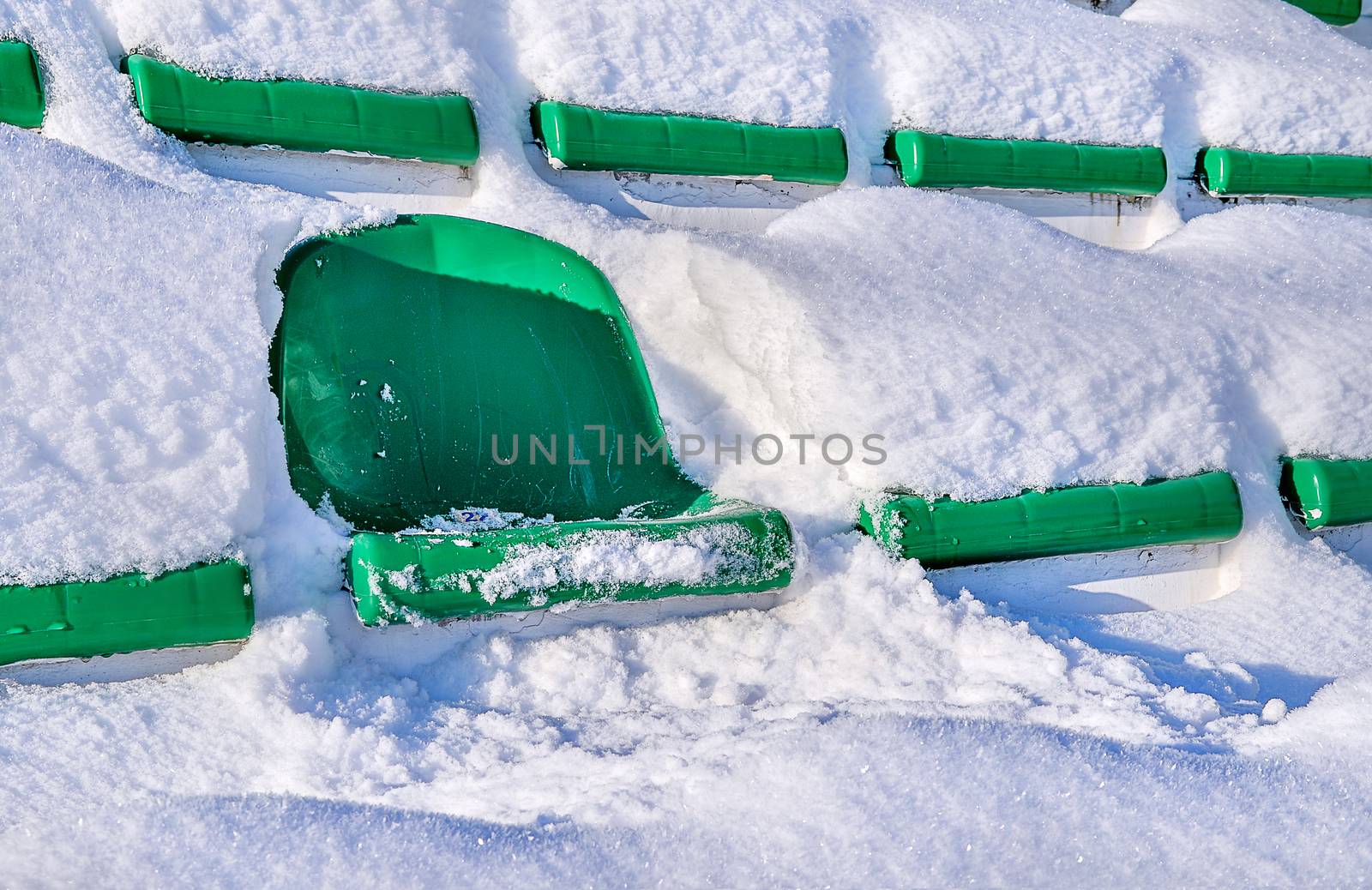 Green seats of a sports stadium, covered with snow. The concept of closing the summer season of games