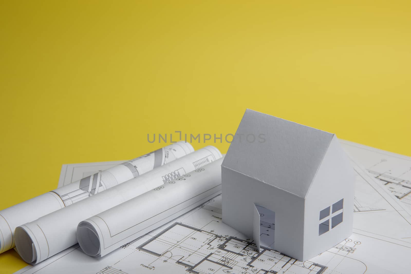 White family paper house, house projects plan and blueprints on yellow background paper. Minimalistic and simple concept, style. Vertical orientation.