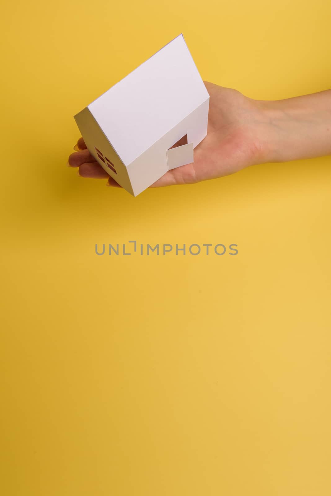 White family paper house in man hand on yellow background paper. Minimalistic style. Copy space. View from above. Horizontal orientation