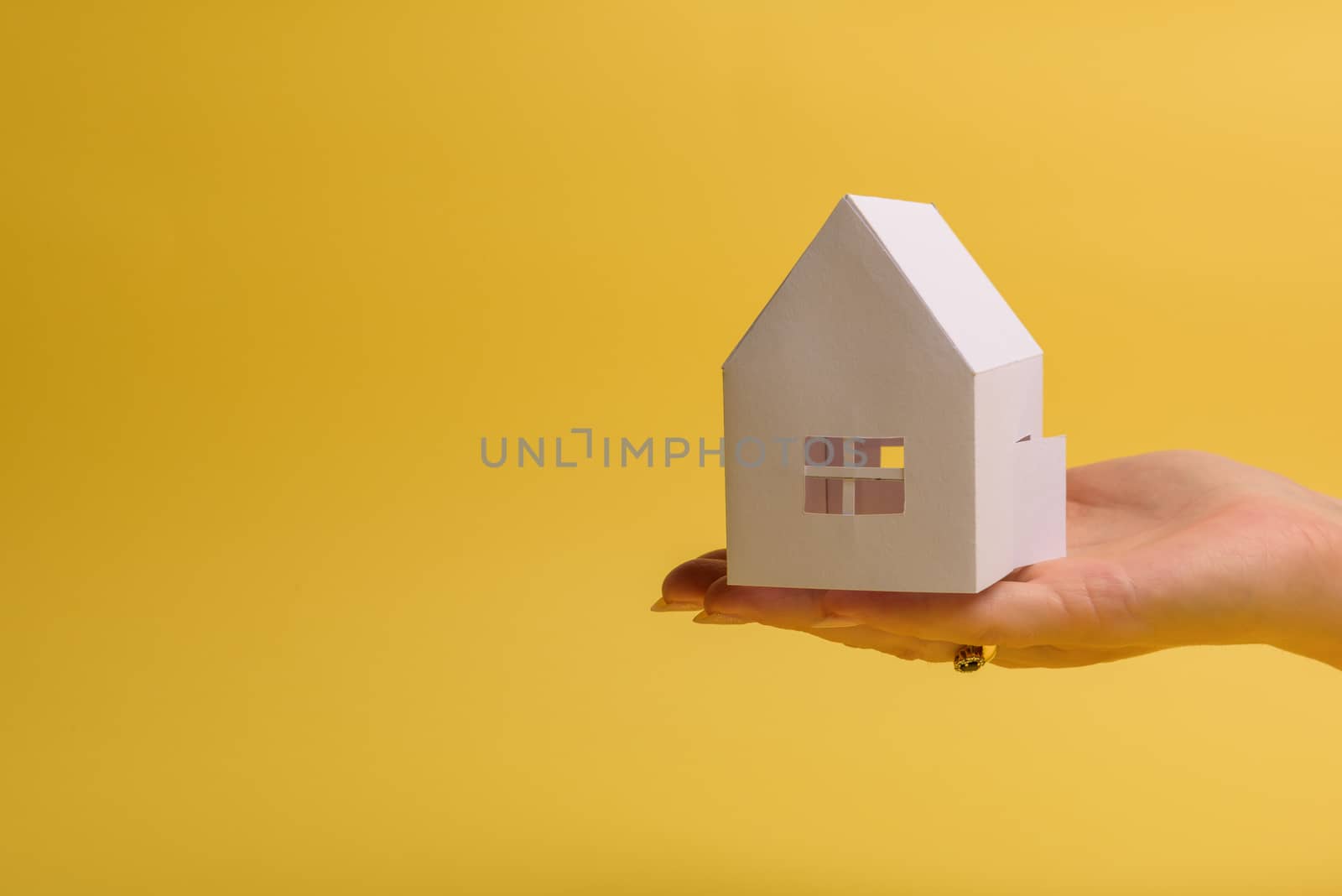 White family paper house in man hand on yellow background paper. Minimalistic style. Copy space. View from above. Horizontal orientation