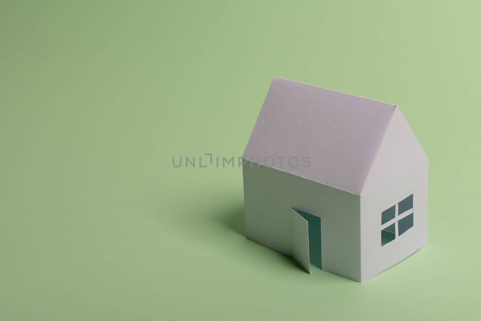 White family paper house in man hand on mint background paper. Minimalistic and simple concept, style. Copy space. Horizontal orientation