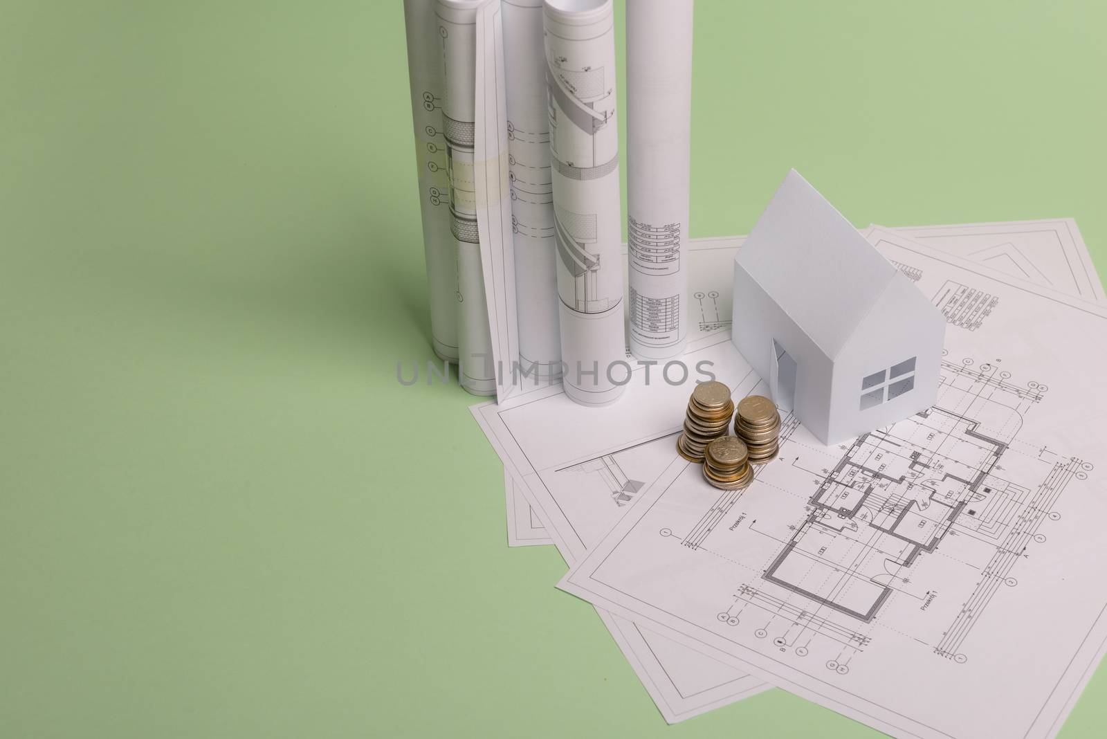 White family paper house , stack of money coins, house projects plan and blueprints on mint background paper. Minimalistic and simple concept, style. Horizontal orientation