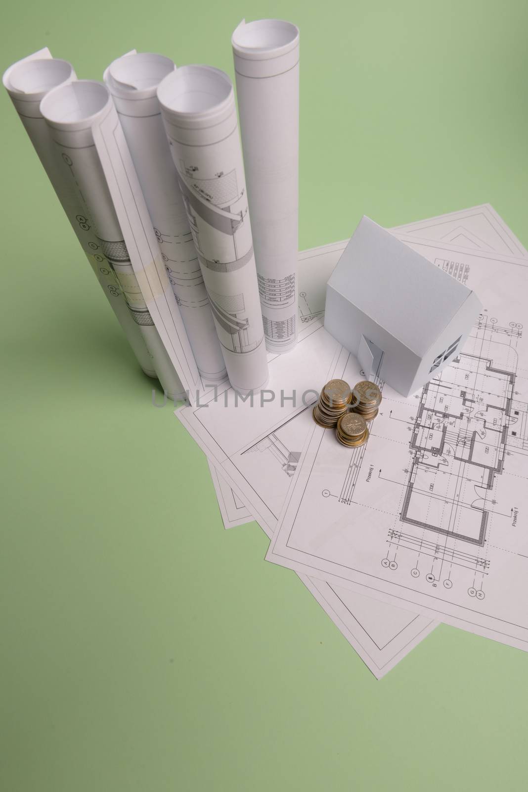 White family paper house , stack of money coins, house projects plan and blueprints on mint background paper. Minimalistic and simple concept, style. Horizontal orientation
