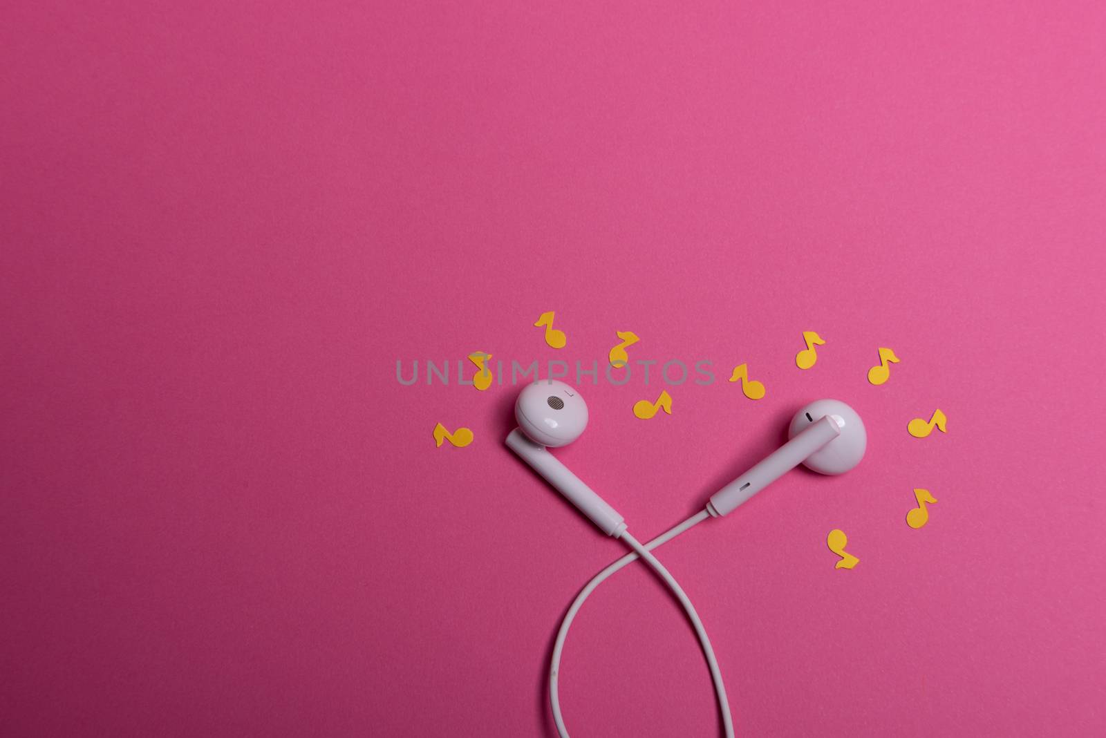 white earphones and yellow paper notes on pink background. view from above