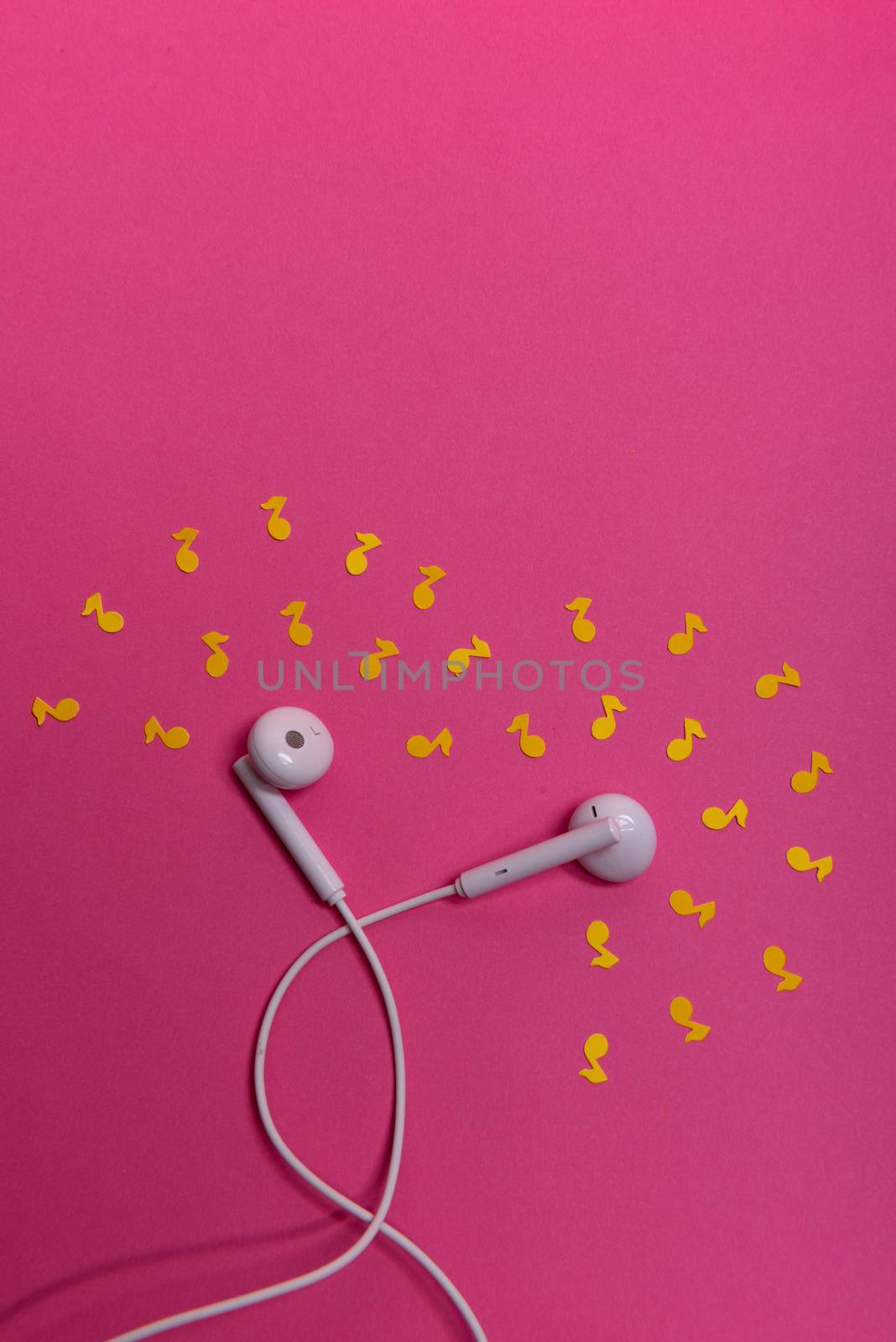 white earphones and yellow paper notes on pink background. view from above