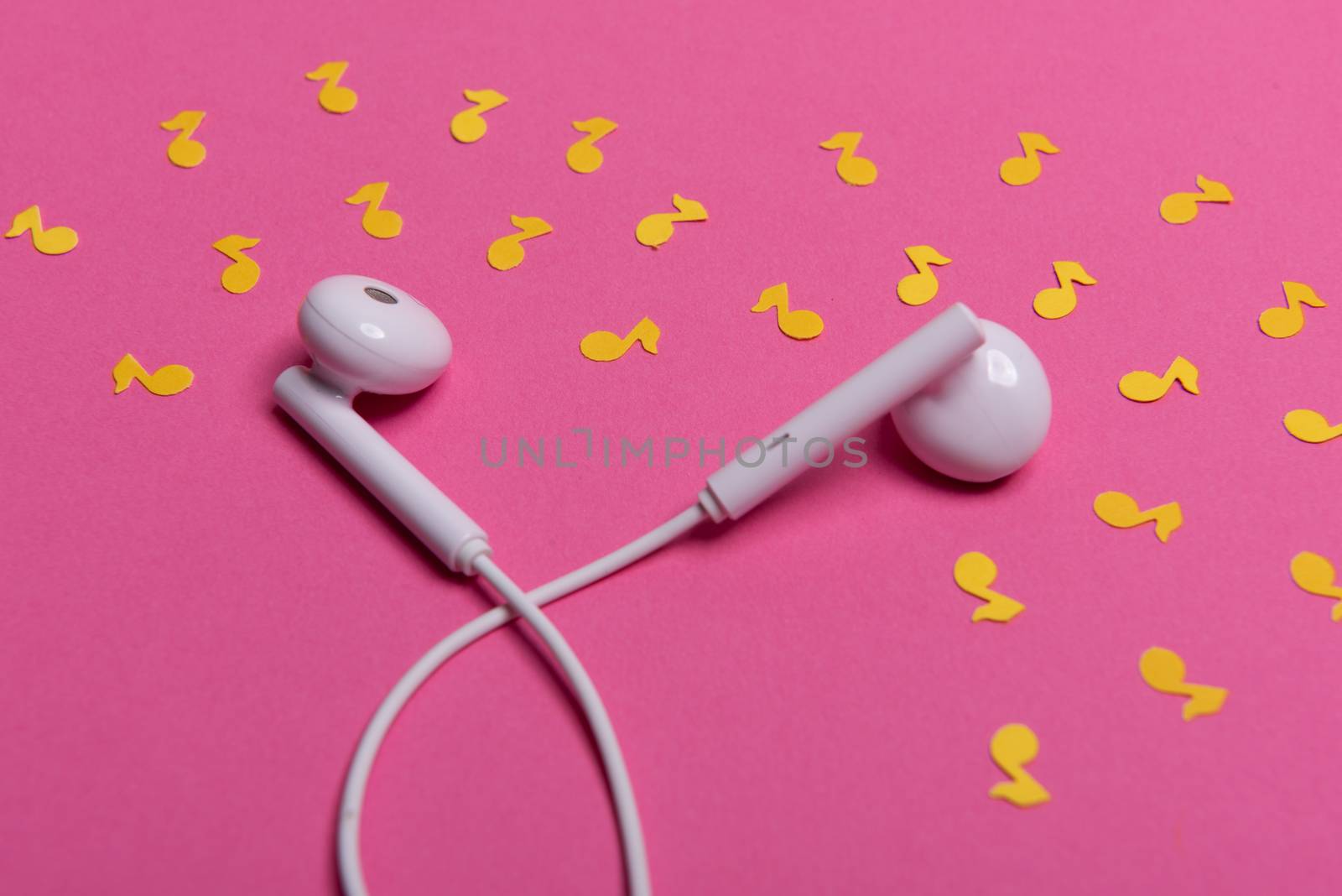 white earphones and yellow paper notes on pink background. view from above