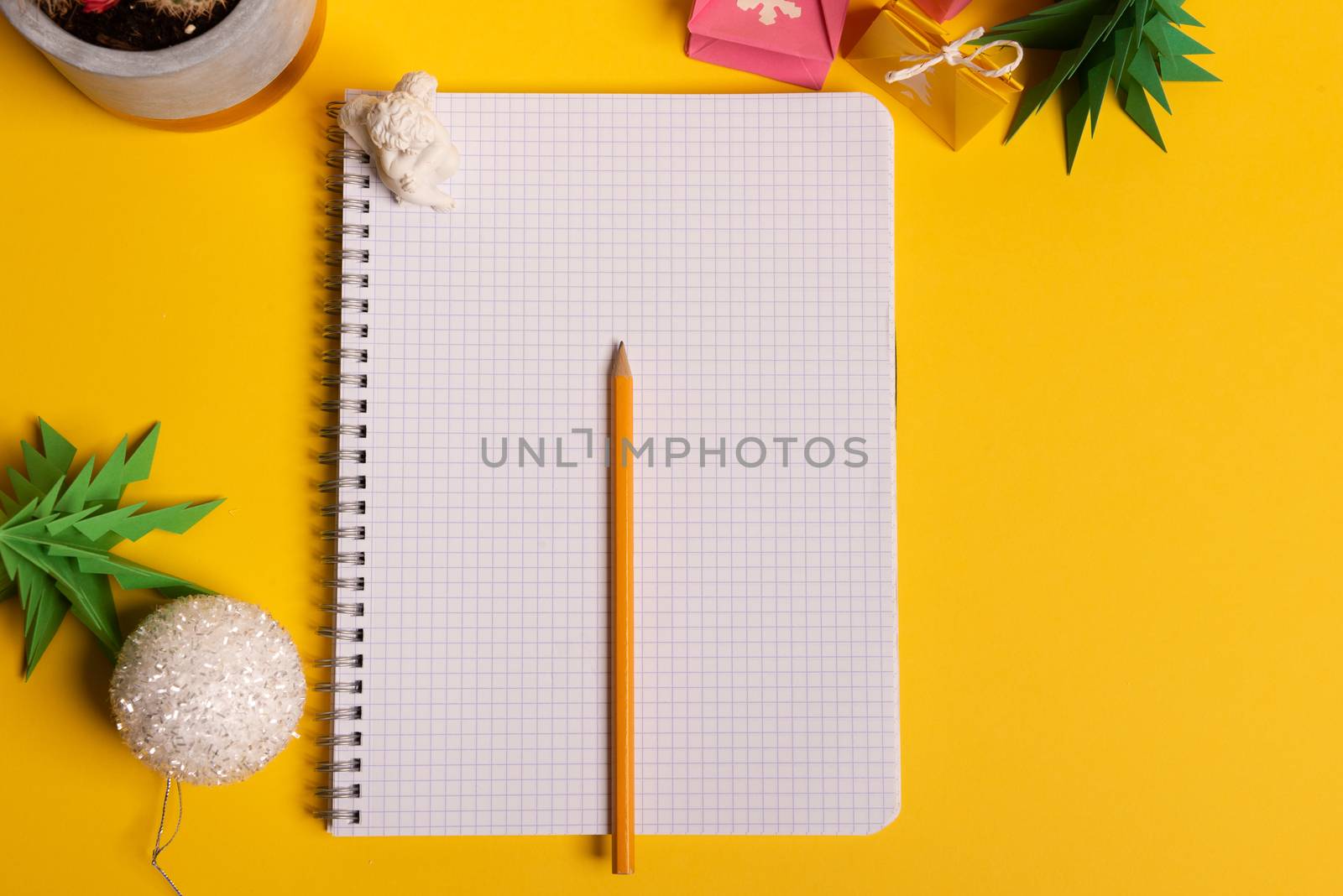 gift box and green origami trees with notepad on yellow desk, table
