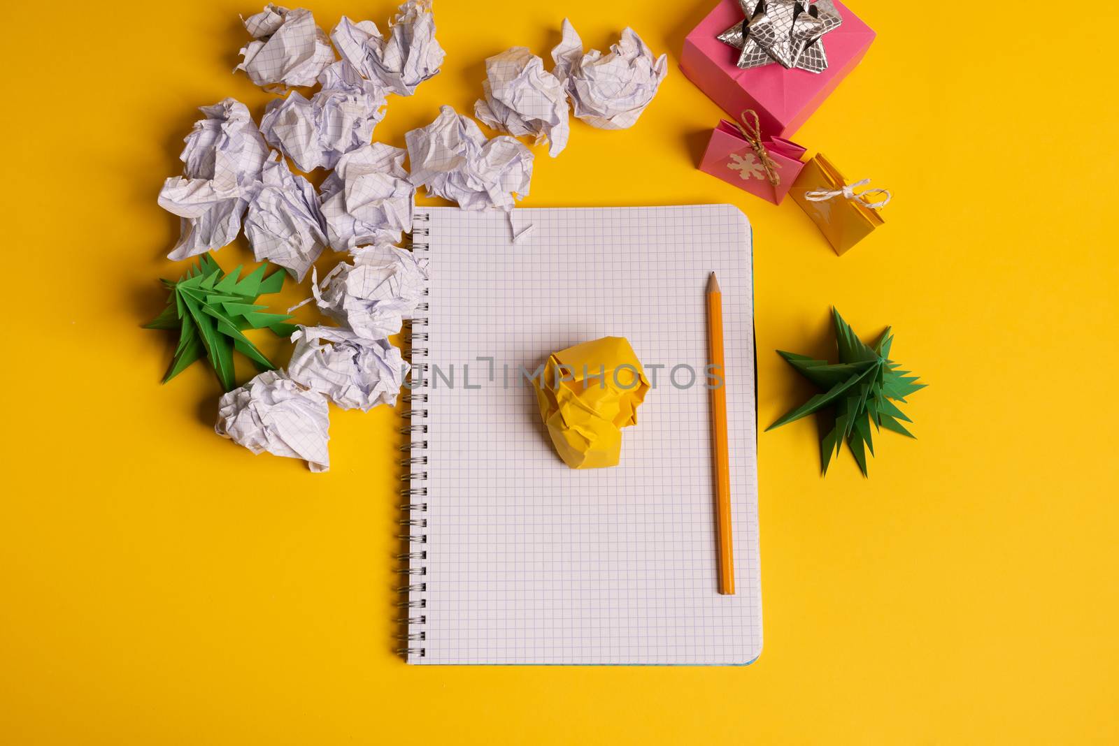 gift box and green origami trees with notepad on yellow desk, table