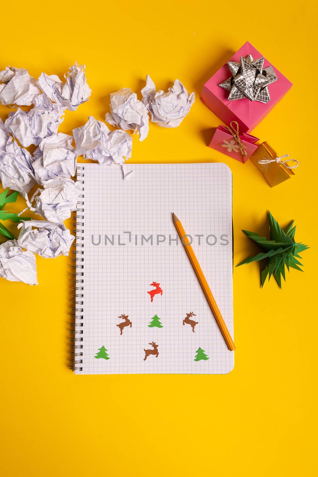 gift box and green origami trees with notepad on yellow desk, table