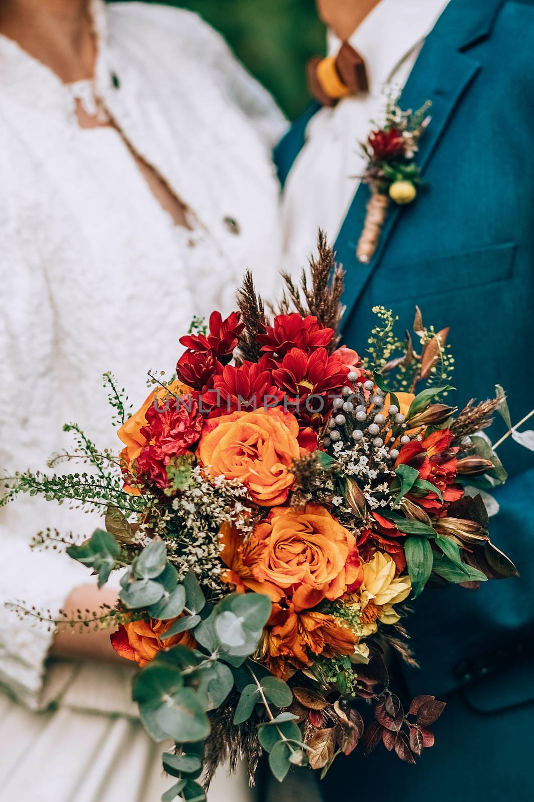 Crop blurred just married couple in elegant clothes hugging and holding beautiful bouquet of fresh colorful flowers in composition with green and brown herbs